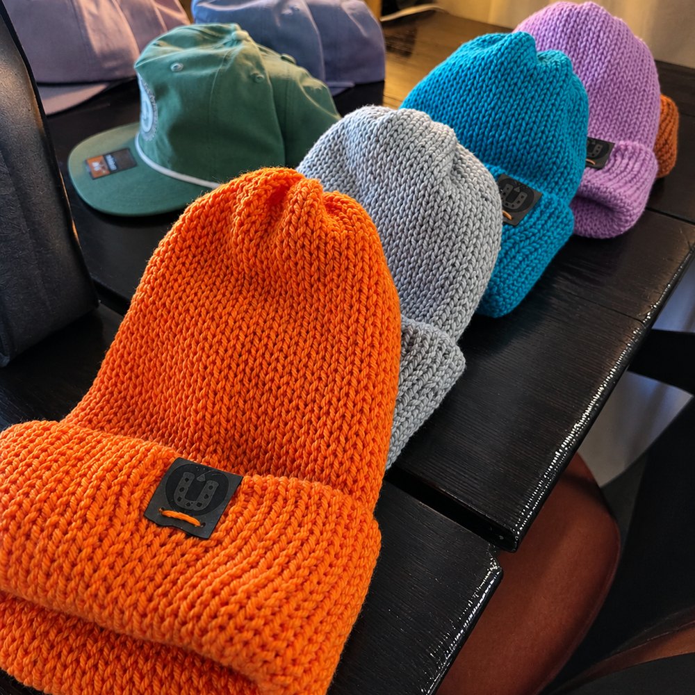 Hand-knitted beanies in orange, grey, blue and purple with the horseshoe tag