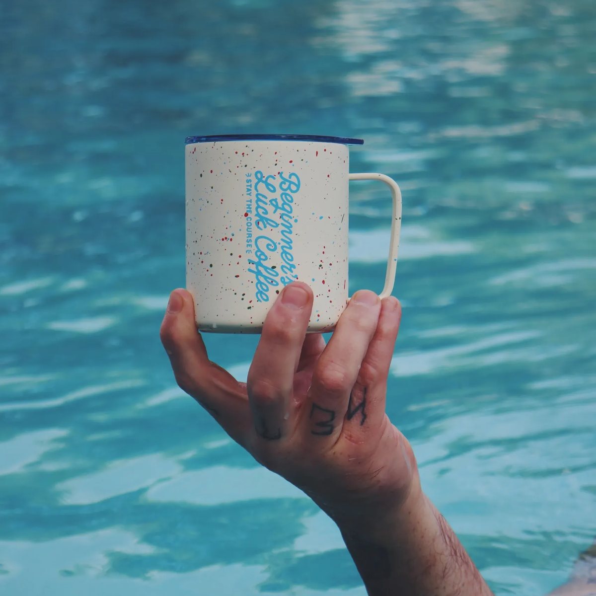 Beginner's Luck Coffee camp mug held above a pool
